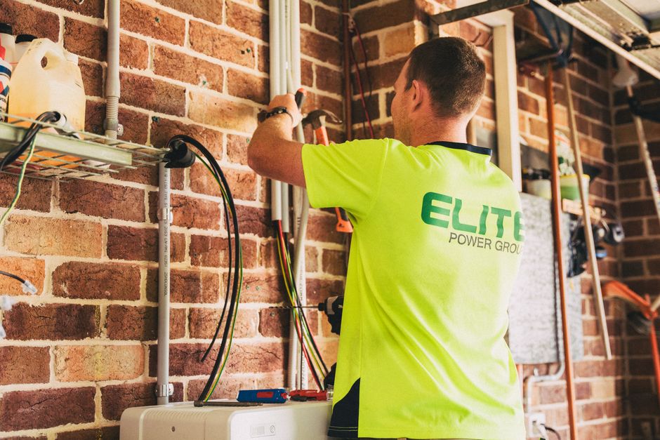 Elektrikár inštaluje moderné batériové úložisko na stenu rodinného domu.